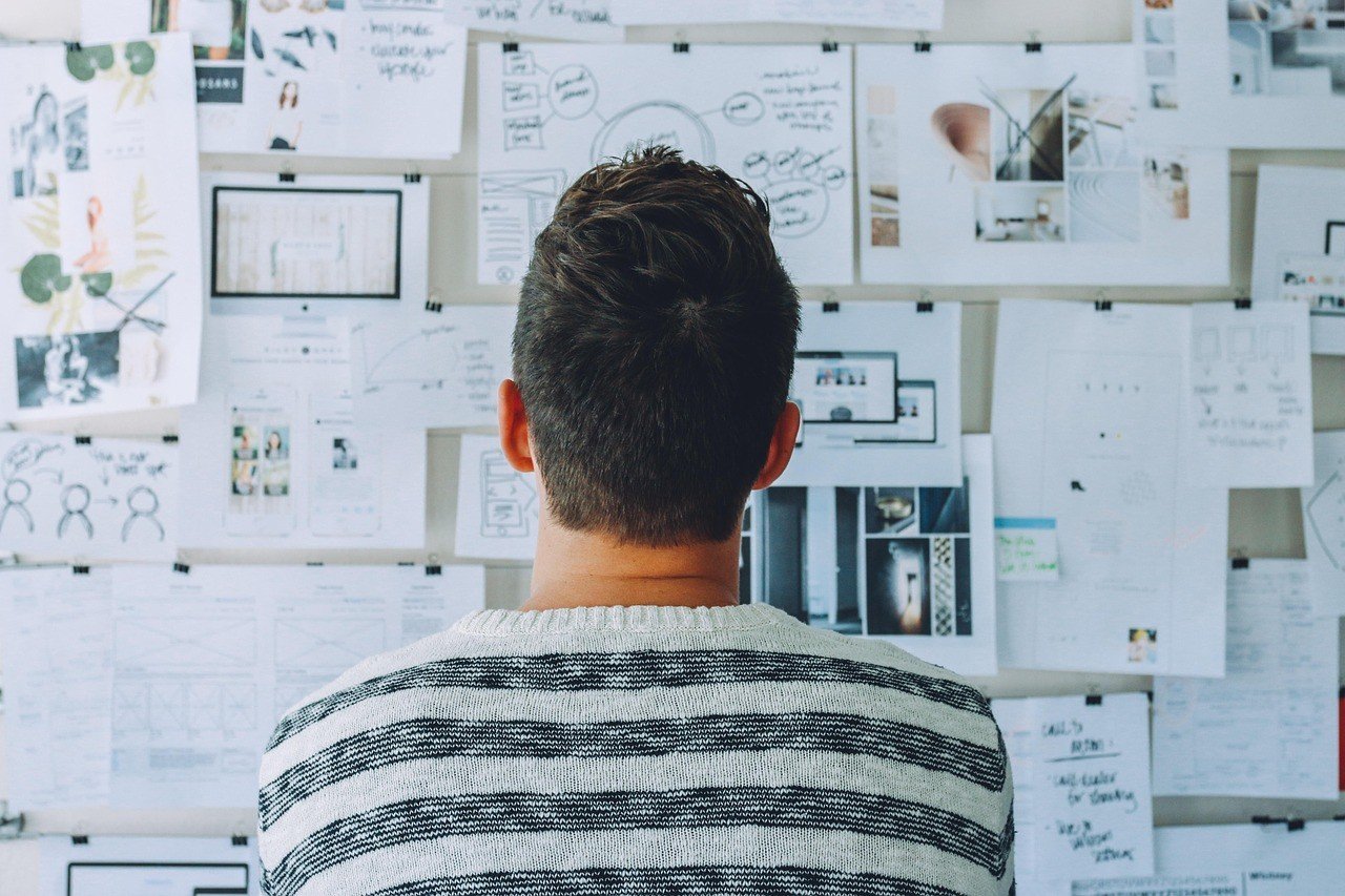 Person von hinten vor einem Whiteboard mit Skizzen und Konzeptnotizen in einem Workshop-Setting